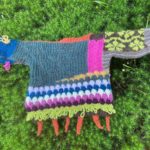 brightly colored, many textured back of baby sweater-dangling carrots and green vines. on a backdrop of star moss