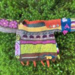 brightly colored, many textured baby sweater front-deep orange, mustard yellow, fuchsia pinks, blue mixed with earthy browns-with knitted radishes, carrots, blueberries, chanterelle, flowers. on a backdrop of star moss.